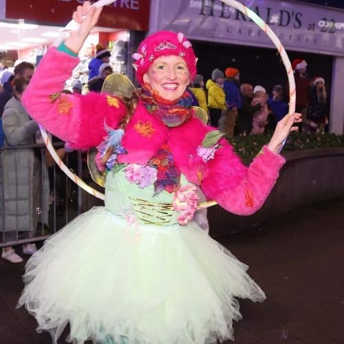 Performer Rachael is in a colourful pink and green fairy costume and holding a hula hoop