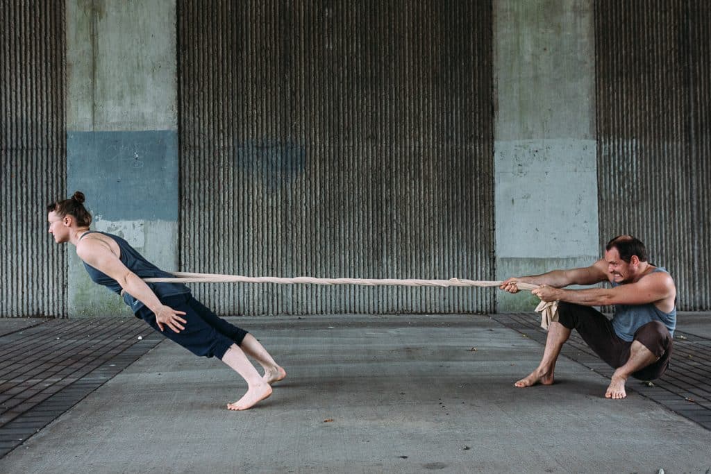 2 people connected by a rope, one leaning away the other pulling