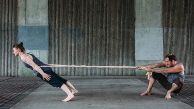 2 people connected by a rope, one leaning away the other pulling