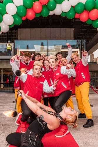 House of Swag dance crew gather behind a shocked and smiling Jedward, while hoopixie is front and centre on her knees in a Black outfit with a chain chest harness, in a slight backbend with fire poi spinning in front of her face.