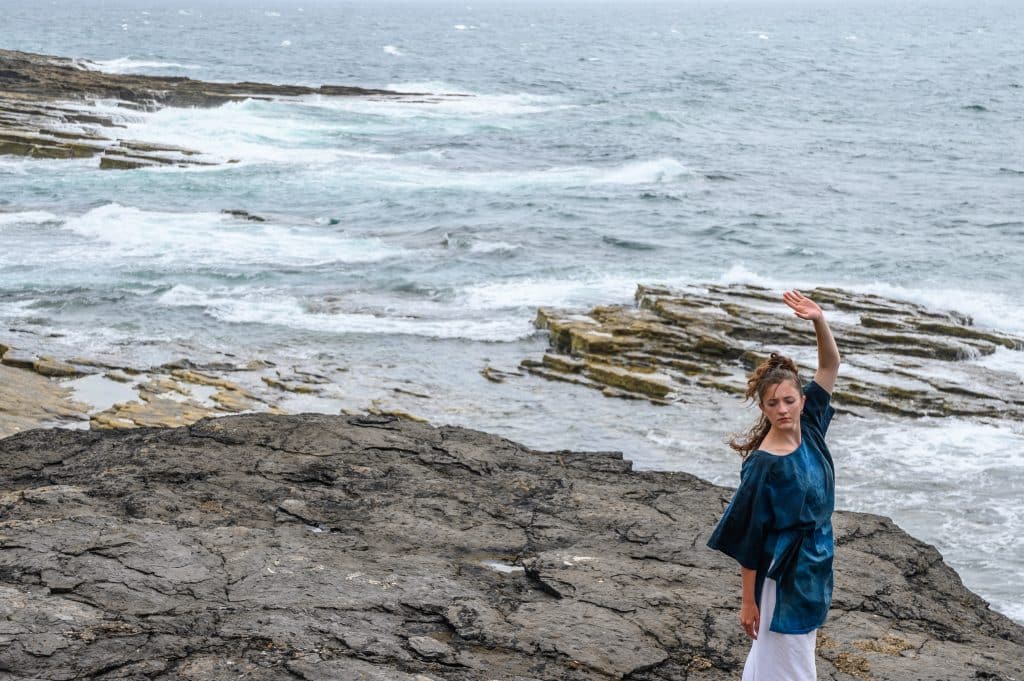 1 performer dancing on the rocks by the sea and one playing cello