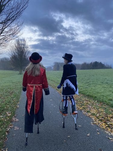 Two young performers on stilts walk into a misty early morning
