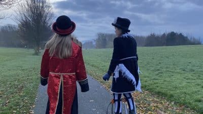 Two young performers on stilts walk into a misty early morning