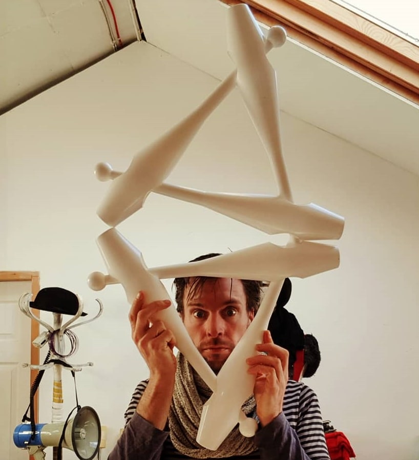 A man looking through juggling clubs which he is balancing.